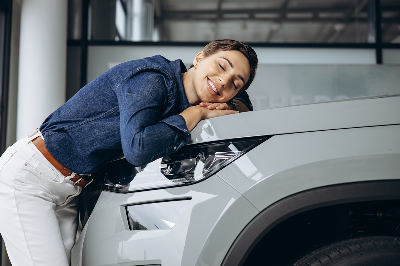 Mulher feliz, abraçando seu veículo, para representar a satisfação do cliente ao utilizar os serviços de vitrificação ou cristalização para conservar a pintura do carro como nova