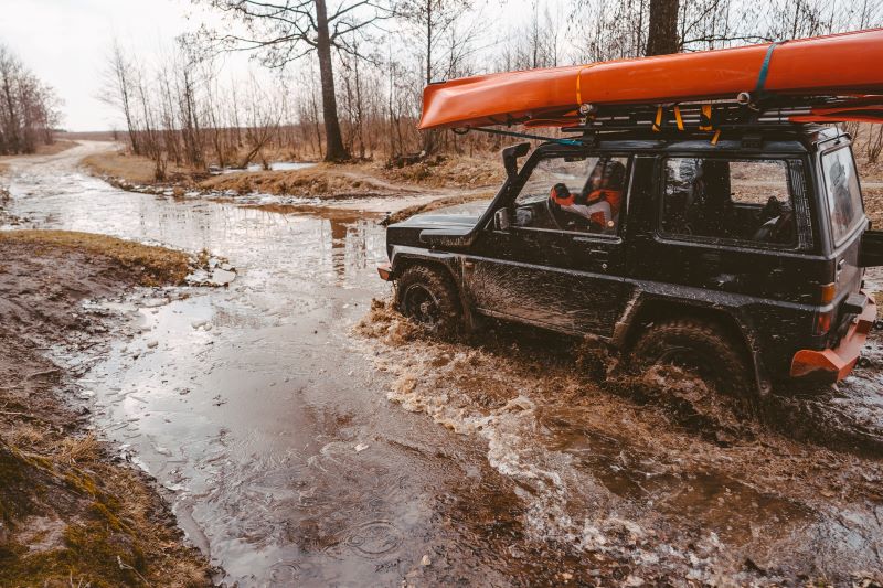 Motorista fazendo trilha em um ambiente cheio de terra e água dentro usando um jeep; veículo off-road.