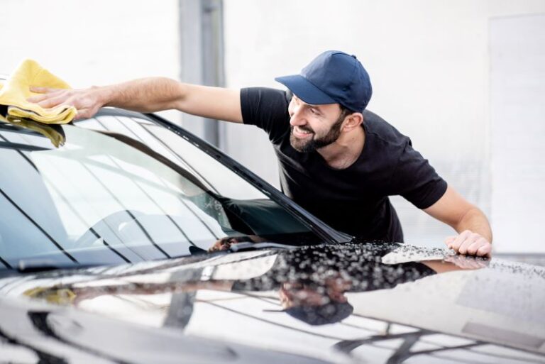 Homem sorridente limpando o para-brisa do carro durante a higienização de veículos.