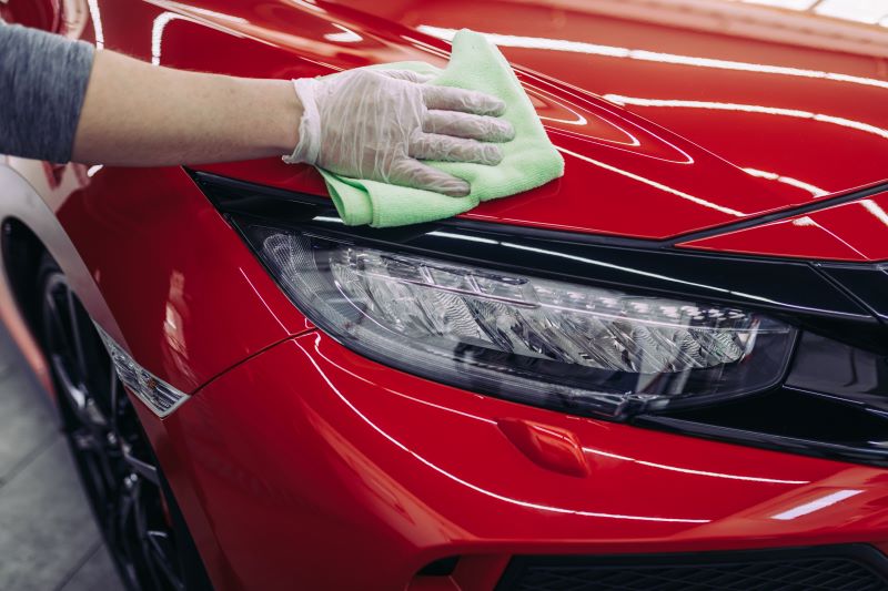 Mão passando flanela em automóvel vermelho brilhoso que acabou de sair do polimento de carros.