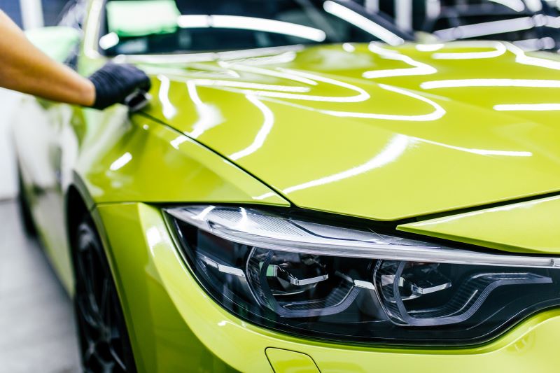 Produtos para estética automotiva: mão limpando carro amarelo com luva e equipamento adequado.