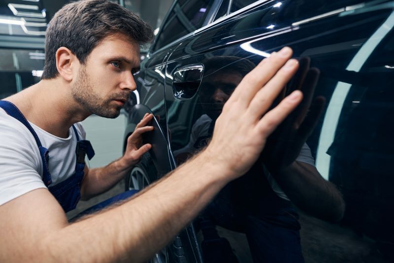 Como tirar arranhões de carros: profissional verificando arranhão em porta de carro preto.