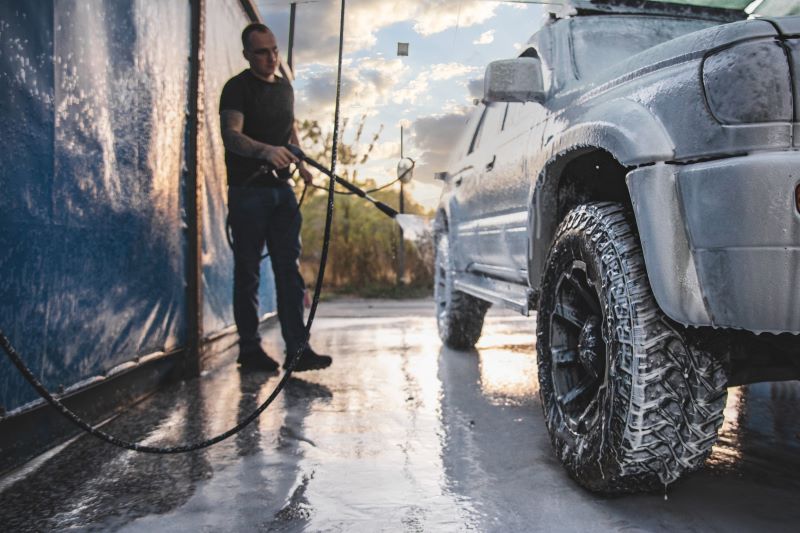 Lavagem automotiva​: homem lavando o carro com mangueira.